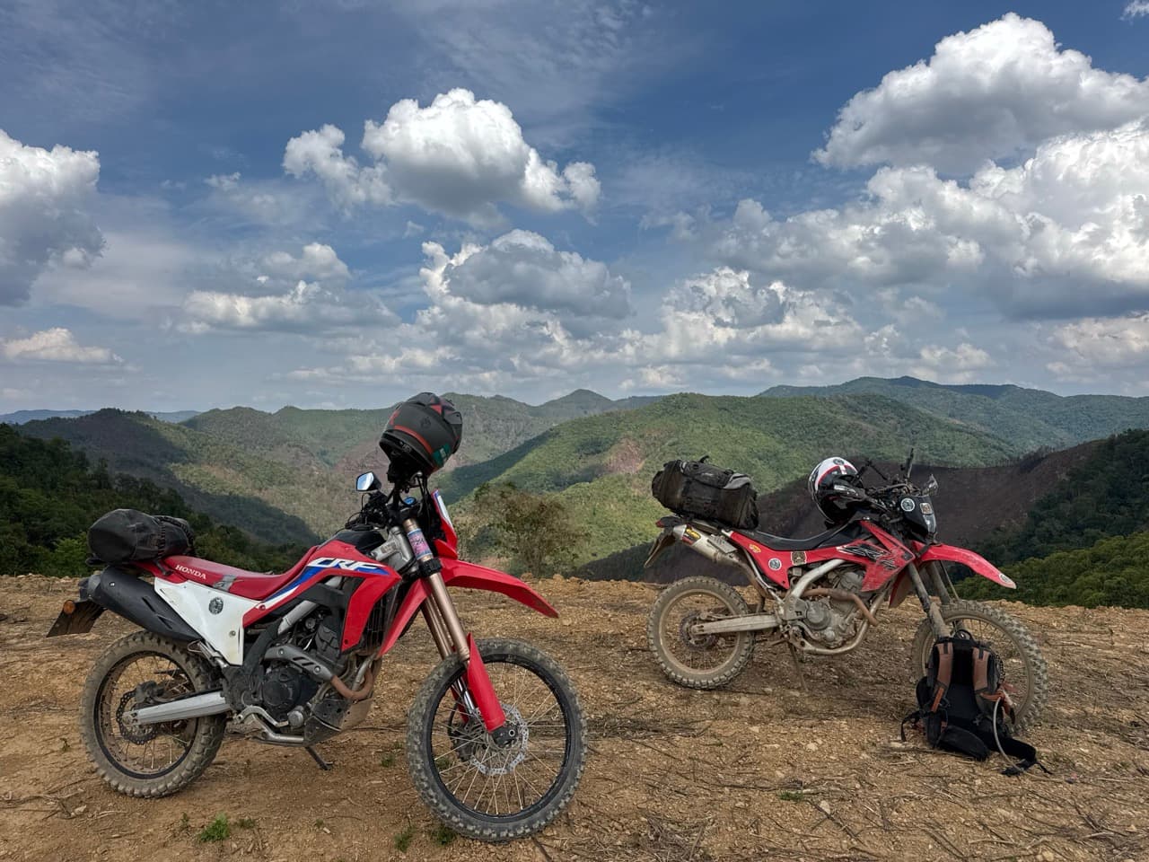 Two Honda CRFs parked on a mountain ridge between Om Koi and Mae Sariang with a panoramic view of layered mountains